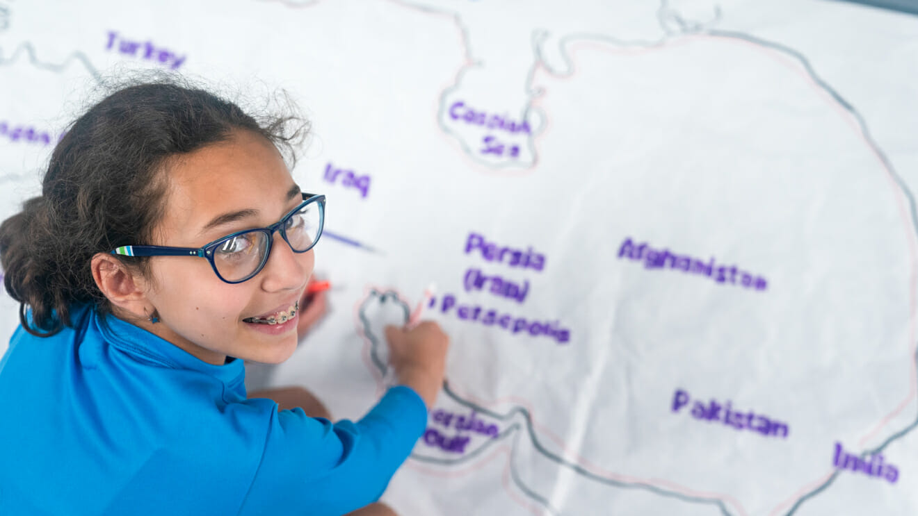 Smiling girl looks up from drawing large map of Persia
