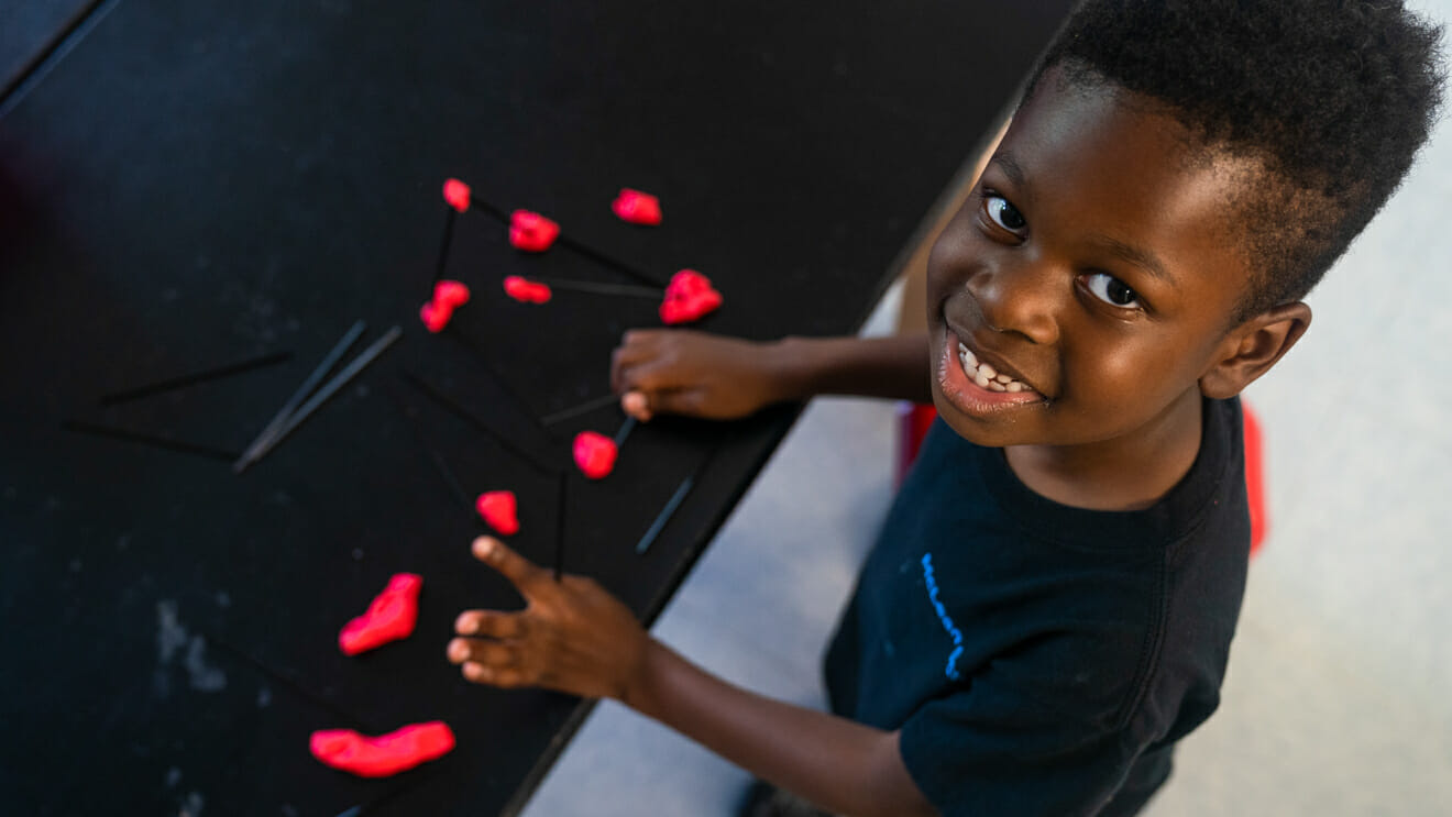 Smiling boy looks up from model putty and sticks