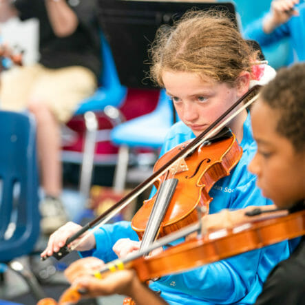 Students play violins in orchestra