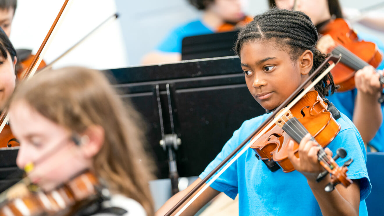 Young girl plays violin in orchestra