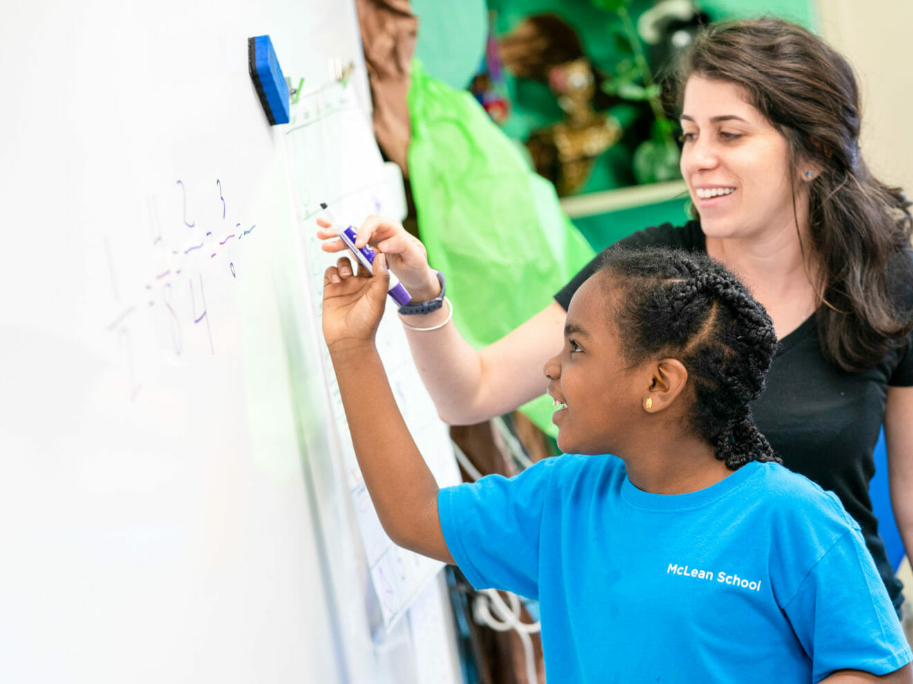 Teacher helps girl write on whiteboard in class