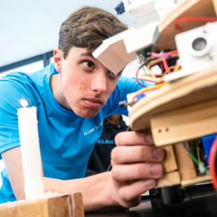 Upper school boy leans down to look at robotics