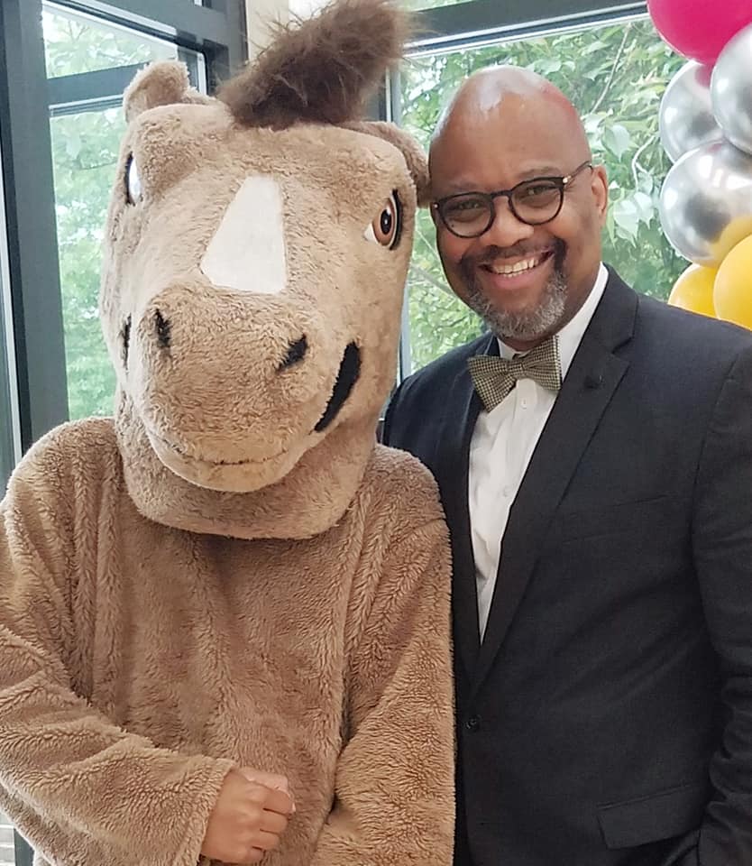 Bobby Edwards, the Director of Community Inclusion and External Relations at McLean, smiling while posing with McLean's Mustang mascot