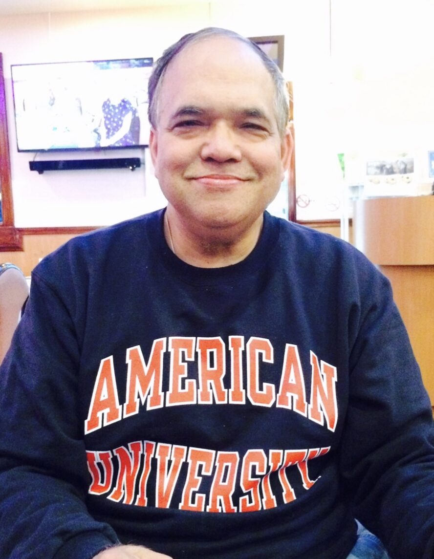 Rajiv Gupta, Assistant Accountant at McLean School, smiles in his American University sweatshirt
