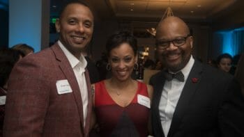two men in suits and a woman in a red dress smiling at a McLean event