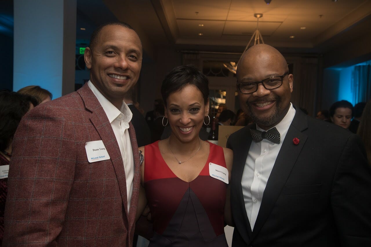 two men in suits and a woman in a red dress smiling at a McLean event