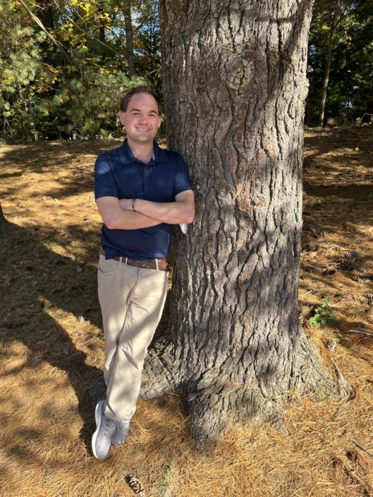 Adam Shepherd, 6th grade teacher at McLean School, smiles at camera while leaning against a tree