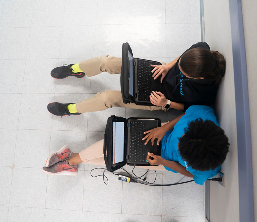 Two students sitting in a hall on their laptops.