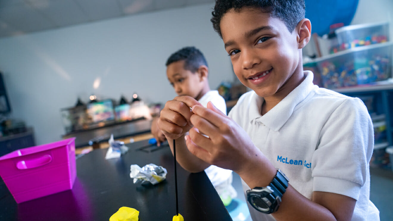 Smiling boy builds model with sticks and putty