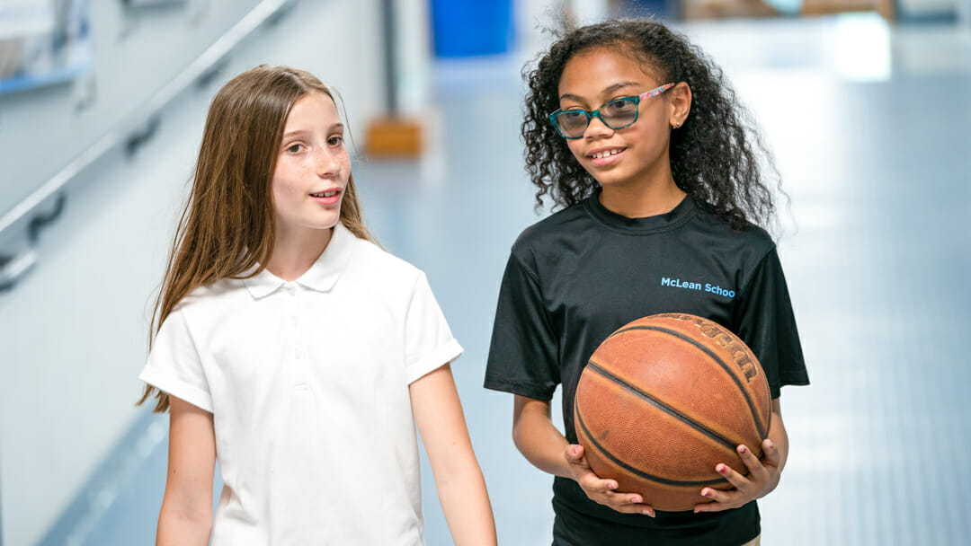 Two girls walk down hall with basketball