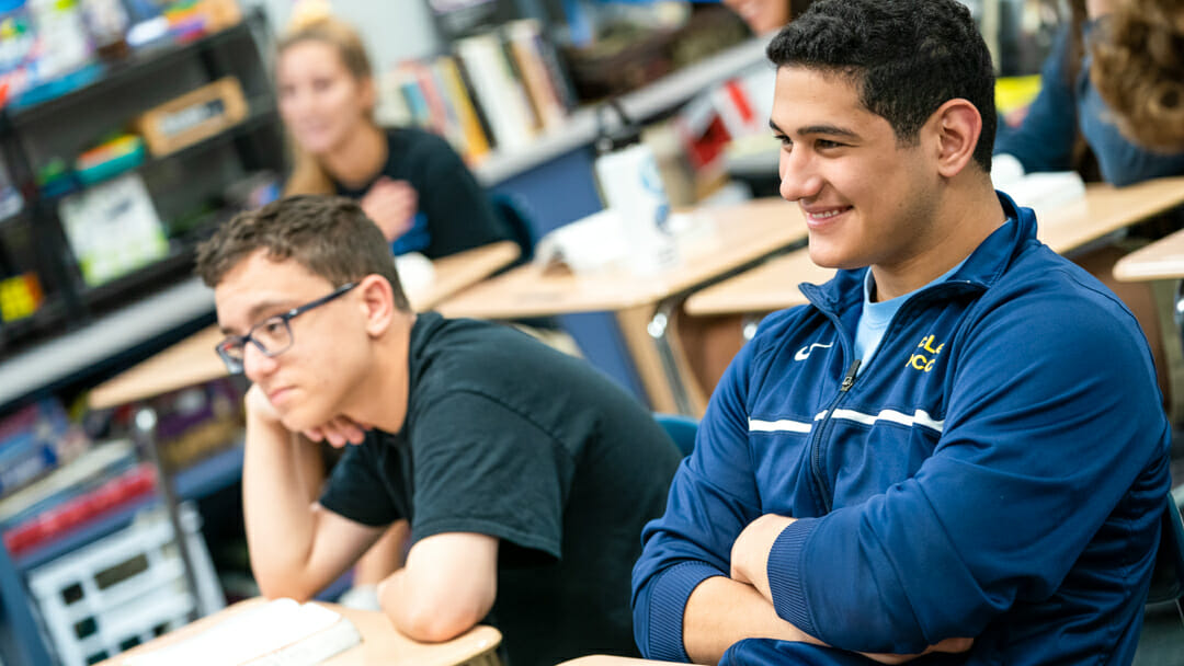 Smiling students sit at desks in classroom