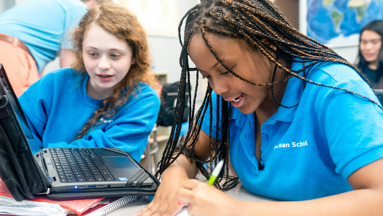 Two girls write while working on a laptop