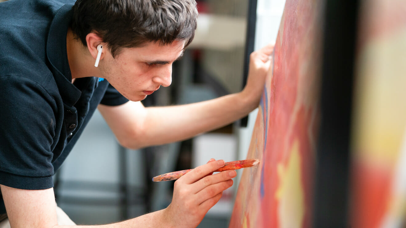 Upper school student leans over large painting