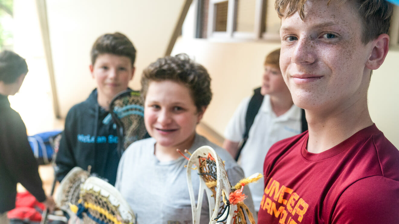 Group of students hold lacrosse sticks in school hallway