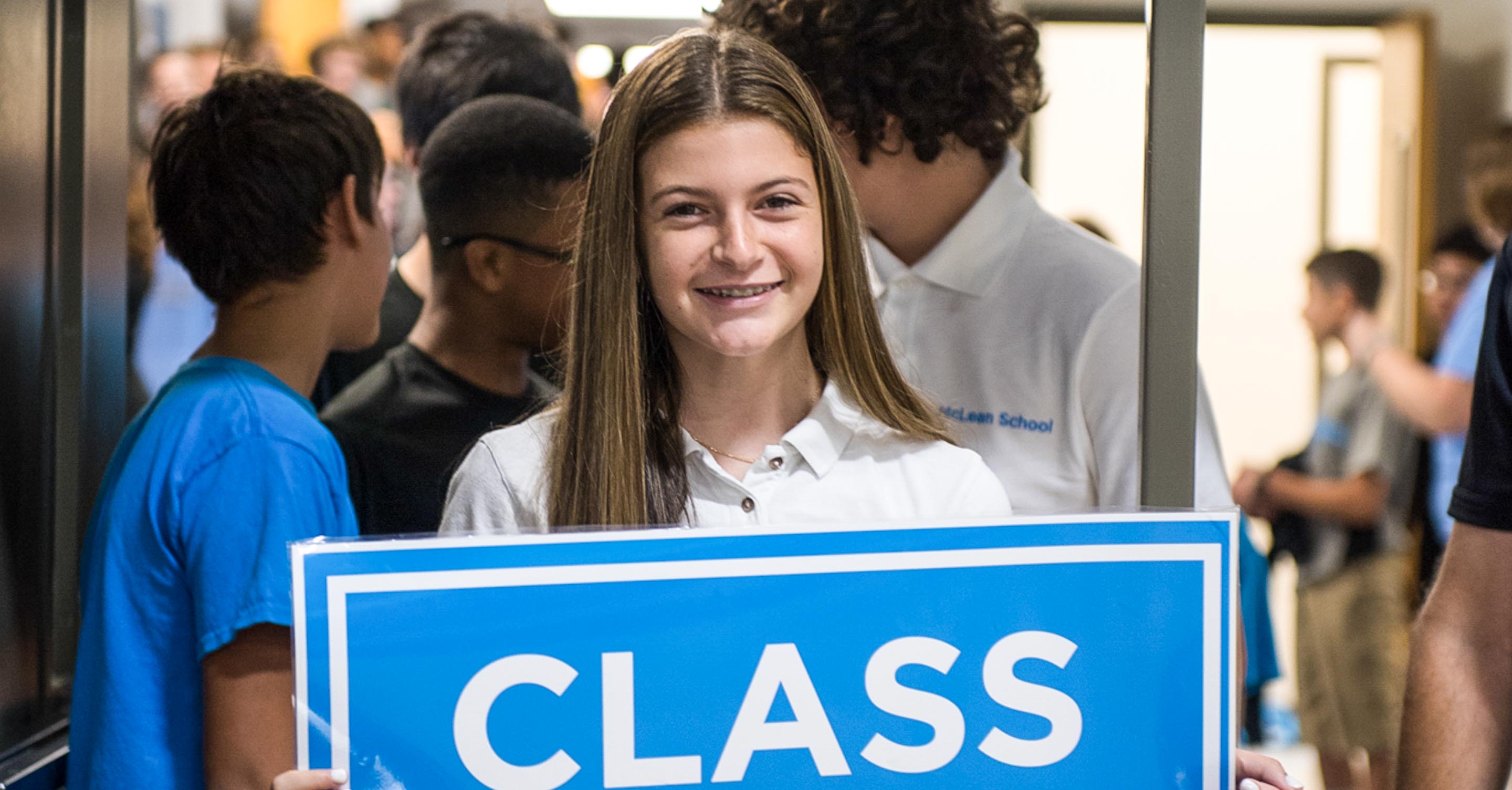 Smiling girl holds sign at school assembly