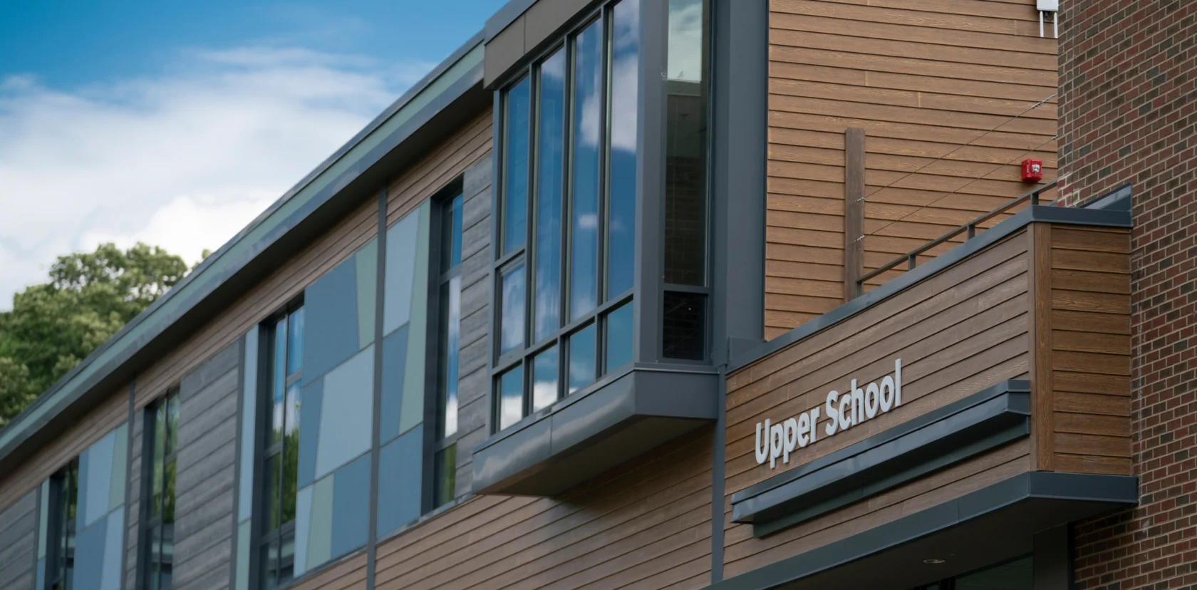 A modern building with wood paneling and large windows displays a sign that reads "Upper School" near the entrance.