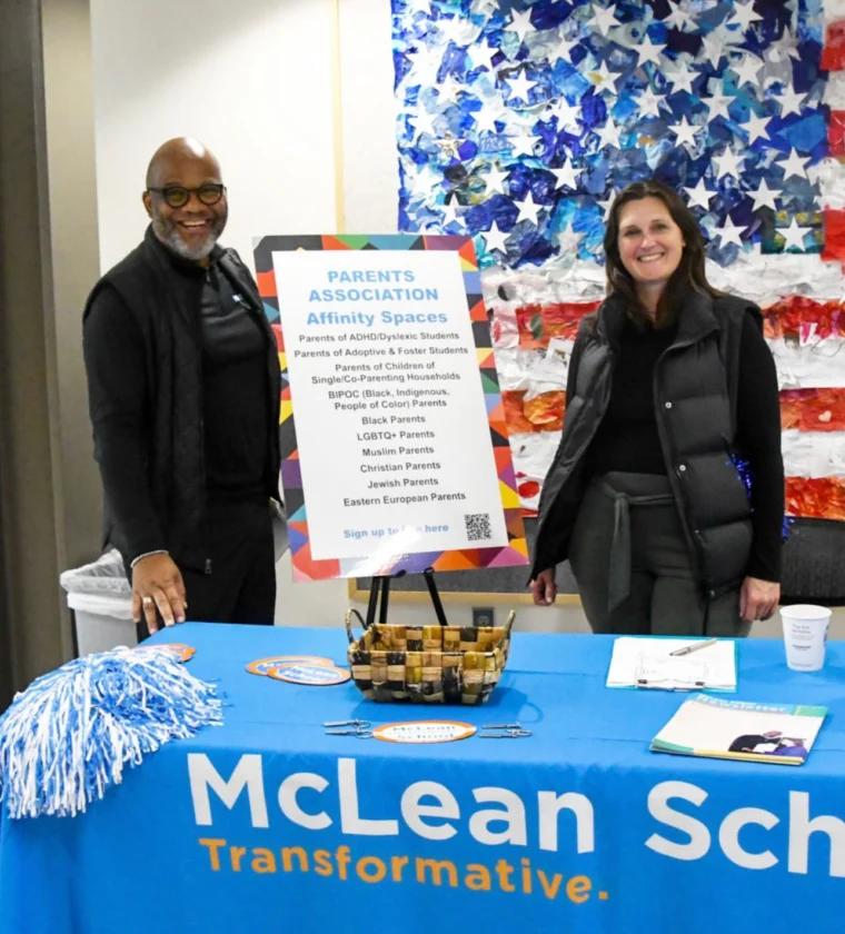 A man and woman standing next to a table with a sign.