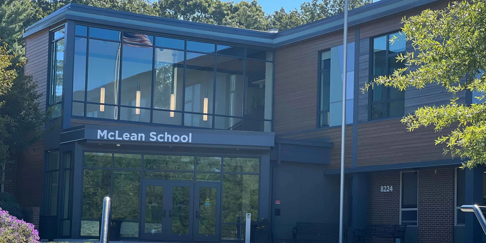 Exterior view of McLean School building with large glass windows, a visible American flag reflection, and the entrance labeled with the school's name.