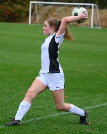 A soccer player in a white and black uniform prepares to make a throw-in during a game on a grassy field.