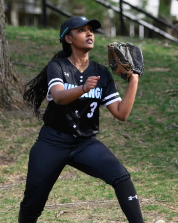 A softball player in a black uniform and glove prepares to catch a ball outdoors on a grassy field.