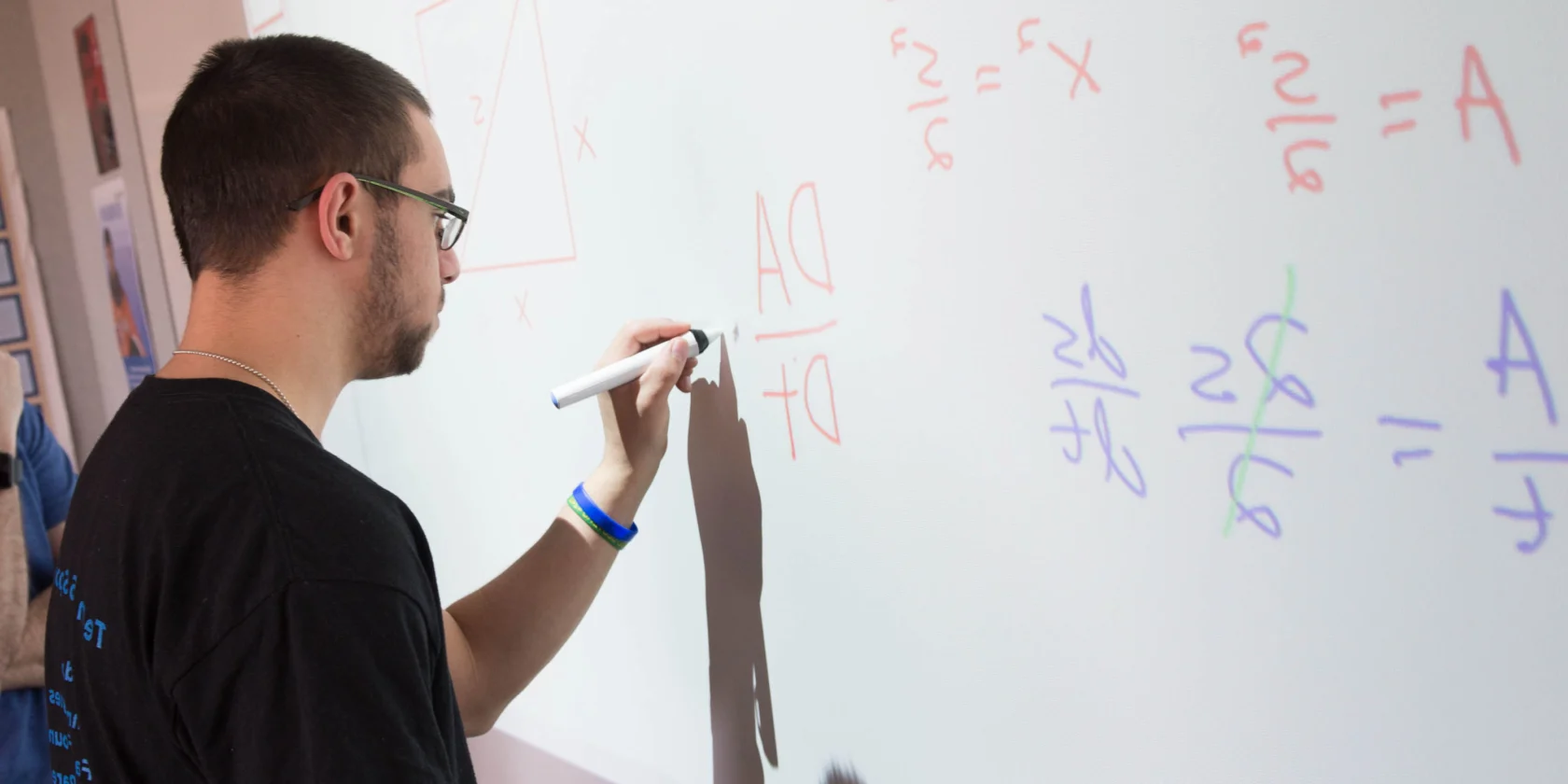 A person writes math equations on an interactive whiteboard using a stylus.