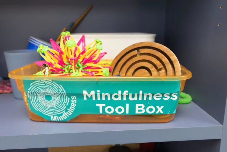 A plastic container labeled "Mindfulness Tool Box" holds various sensory and mindfulness objects on a shelf.