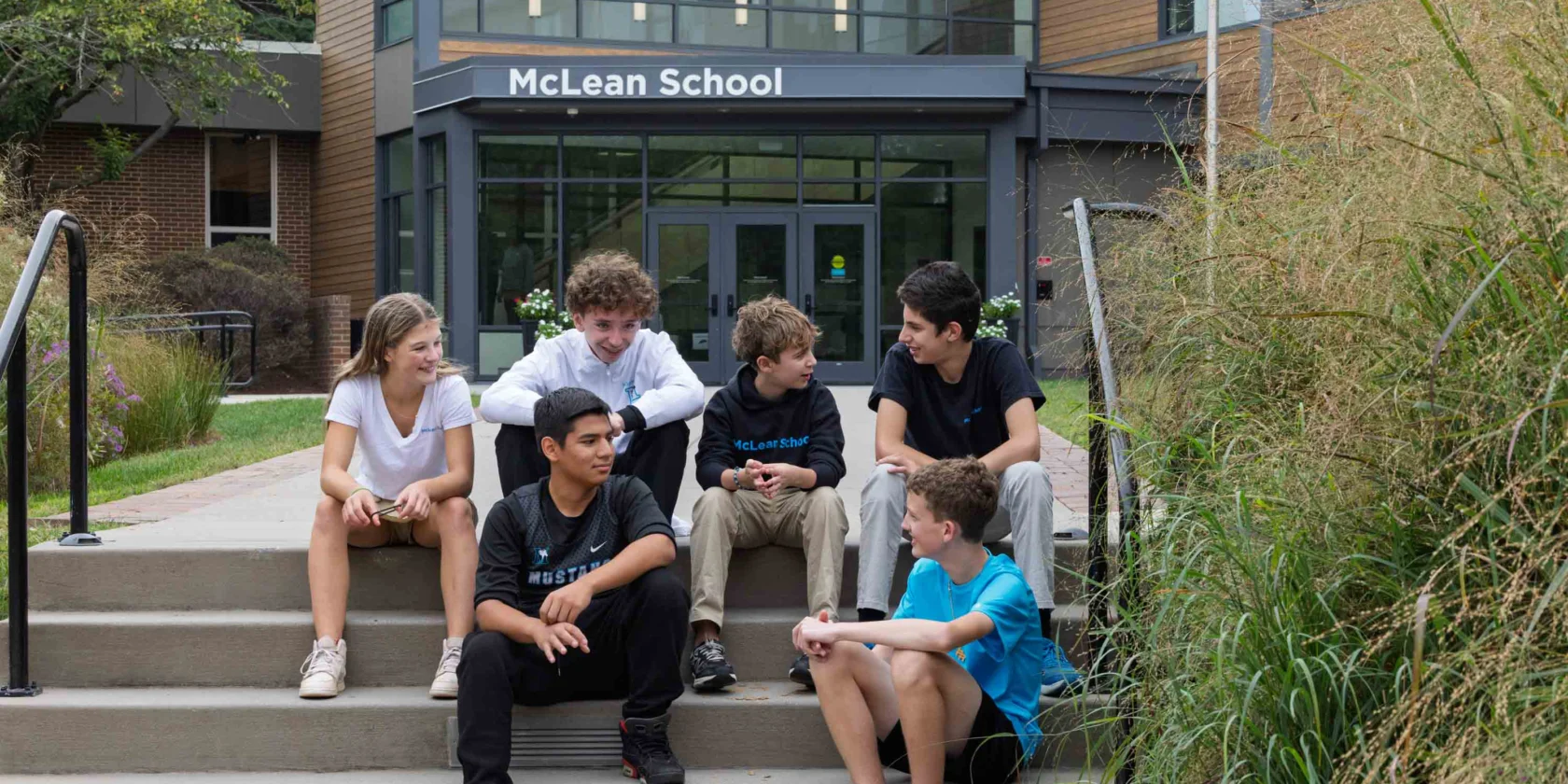 Five students sit and talk on the steps outside McLean School, with the school building visible in the background.