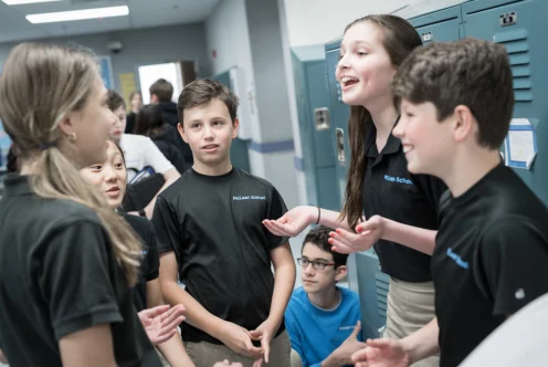 A group of students in school uniforms are talking and smiling together in a hallway near blue lockers.