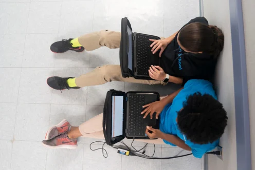 Two students sitting in a hall on their laptops.