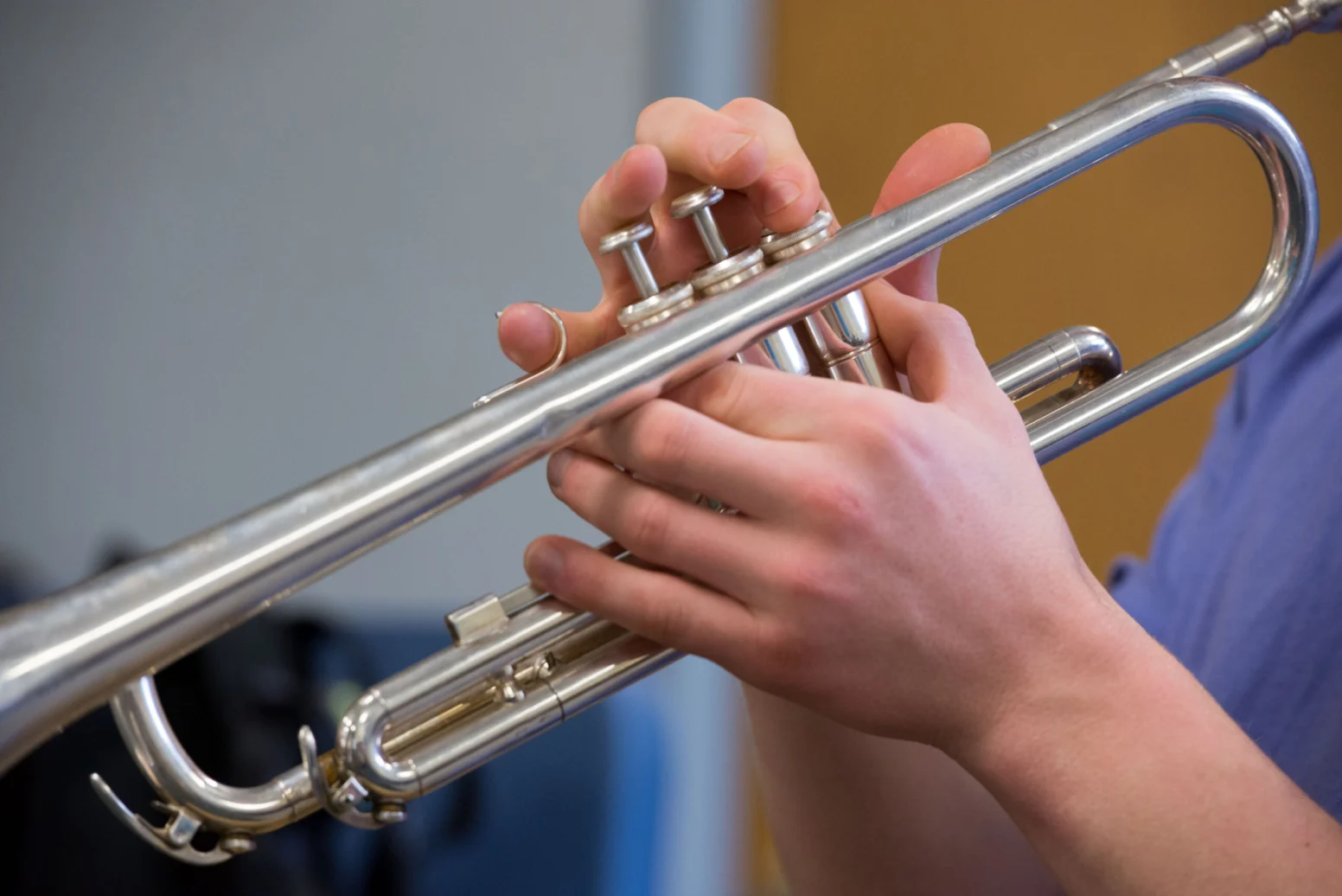 A person holds and plays a silver trumpet, pressing the valves with their fingers.