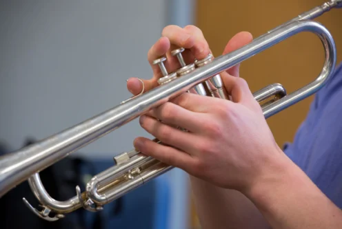 A person holds and plays a silver trumpet, pressing the valves with their fingers.