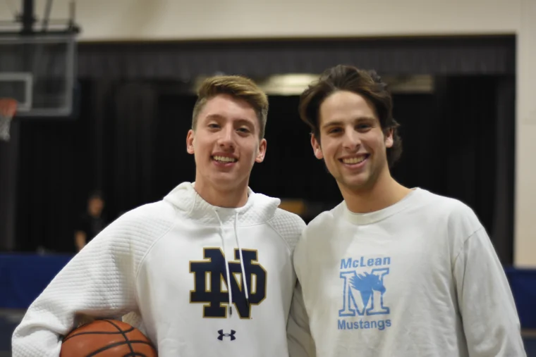 Two young men smile at the camera in a gym. One holds a basketball and wears a Notre Dame hoodie; the other wears a McLean Mustangs sweatshirt.
