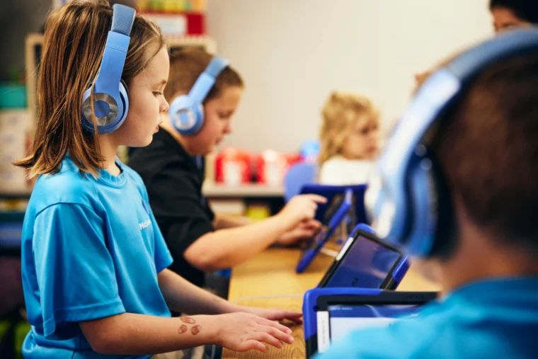 Students wearing headphones and using tablets in a classroom.