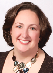 A woman with short brown hair smiles at the camera. She is wearing a dark top and a necklace with large, multicolored oval beads.