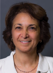Woman with short brown hair, wearing a white collared shirt and small hoop earrings, smiling in front of a plain dark background.