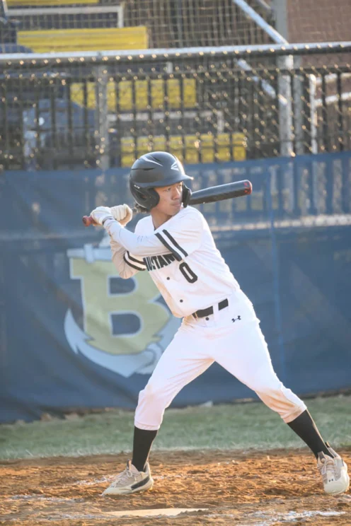 A baseball player in a white uniform and helmet stands in the batter's box, preparing to swing at a pitch during a game.