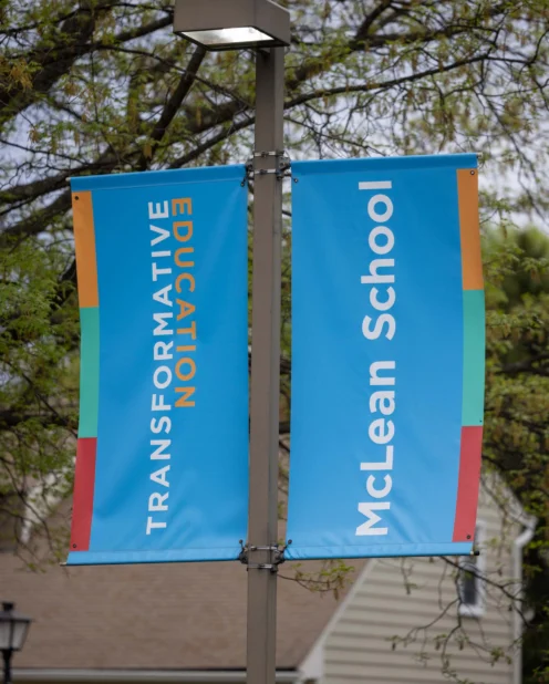 Two blue banners on a pole read "TRANSFORMATIVE EDUCATION" and "McLean School," with houses and trees visible in the background.
