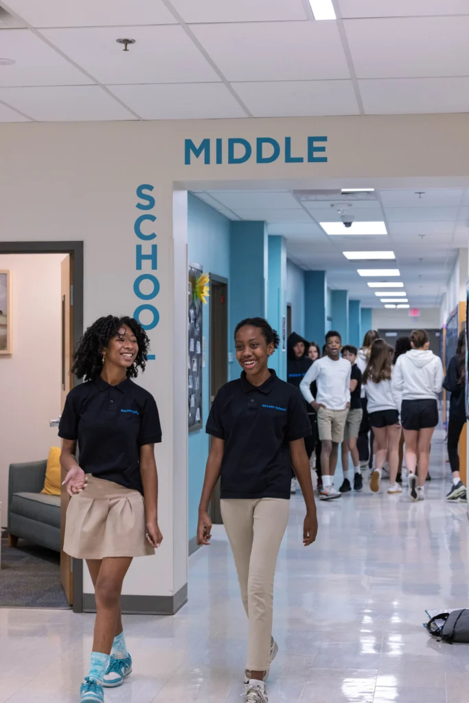 Two students walk down a school hallway under a "Middle School" sign while other students gather in the background.