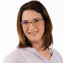 Woman with shoulder-length brown hair, wearing glasses and a light-colored blouse, smiling at the camera against a plain white background.
