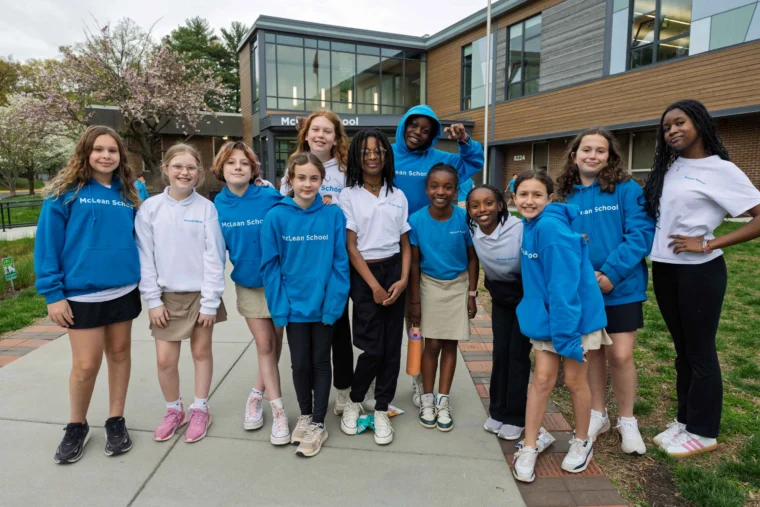 A group of students and one adult pose together outside McLean School, wearing school uniforms and sweatshirts, smiling at the camera.