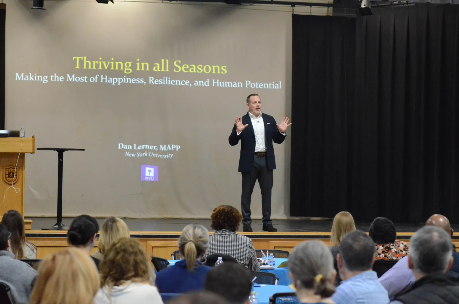 A speaker stands on stage presenting "Thriving in all Seasons" to an audience; presentation slide is visible behind him.