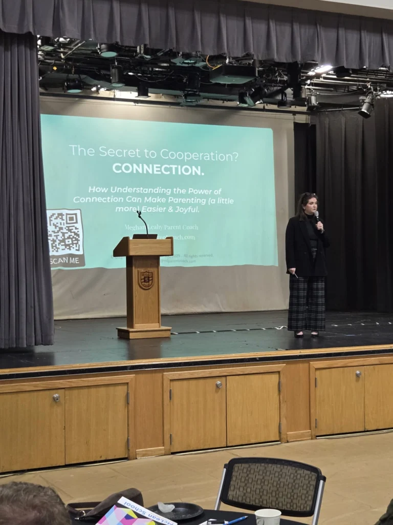 A woman stands on a stage next to a screen displaying a presentation titled "The Secret to Cooperation? Connection" about parenting. A QR code and a podium are also visible.