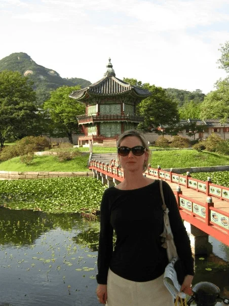 A woman in sunglasses stands before a traditional pavilion at Gyeongbokgung Palace in Seoul.