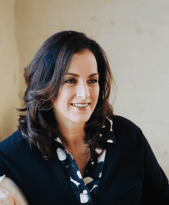 A woman with dark hair wearing a black sweater over a patterned collared shirt.